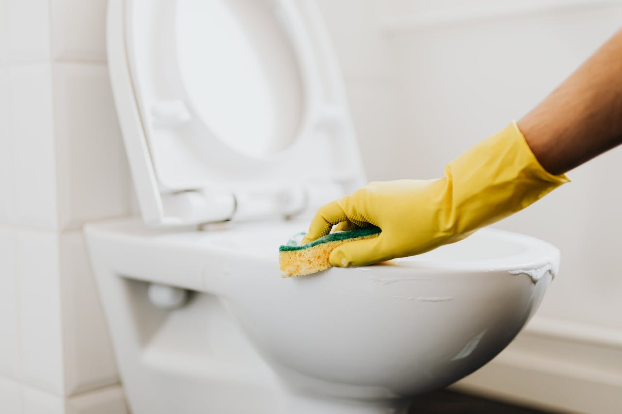why-choose-us A close-up of a hand in a yellow glove cleaning a toilet with a sponge, promoting hygiene.